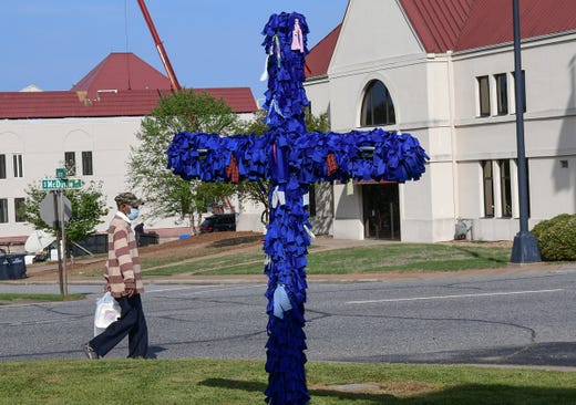 A man wearing a mask walks by St. John's United Methodist Church COVID-19 Cross of Hope in Anderson, S.C. on April 9, 2020. The cross with royal blue ribbons for each diagnosed person in South Carolina started when there were 450 cases, but as the cross was placed in front of the church Thursday morning, the cases in South Carolina are at 2,552 with 63 deaths. 