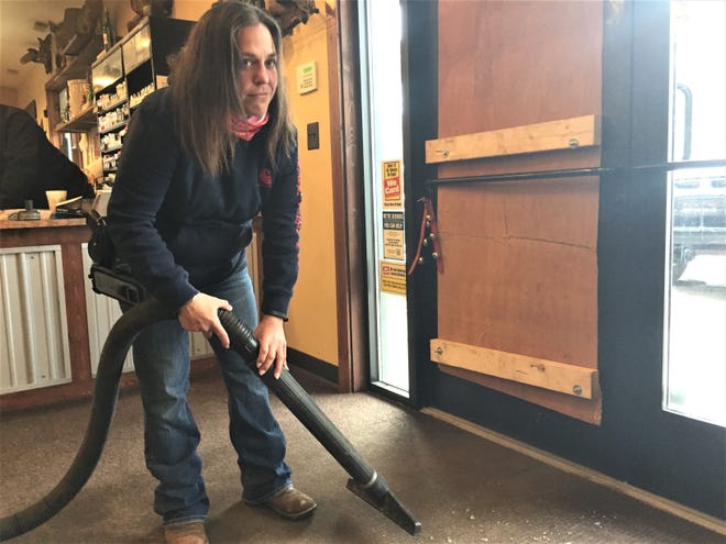 Unadilla Store employee Becky Saylor grimaces as she vacuums up broken glass next to a boarded up entry door, which was smashed. The store was broken in the early morning hours of April 13, 2020.