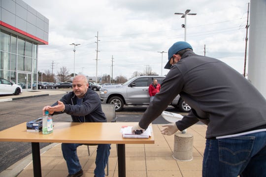 Customer Rony Shikwana, left, applies hand sanitizer after he finishes filling out paperwork, and hands it off to sales manager Matthew Lepior before he takes delivery Tuesday of a 2020 Toyota Tundra at Matick Toyota in Macomb, just days after Gov. Gretchen Whitmer lifted a ban on car sales, but ordered showrooms stay closed. Dealership owner Paul Zimmermann devised using a table in his parking lot to help fill out paperwork.