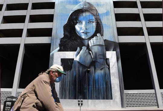 A man wearing a respirator mask rides his bike past a mural in downtown Reno, Nevada on April 13, 2020.