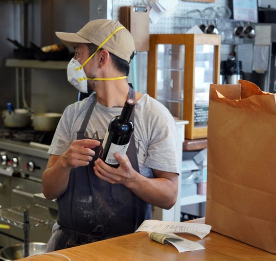 Chef Kris Hammond of Fort Collins, Colorado-based restaurant The Regional, wears an N-95 mask in the kitchen as he inspects wine being sold to a takeout customer.