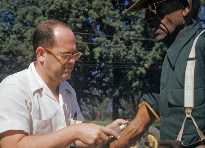 In this 1950's file photo released by the National Archives, a black man included in a syphilis study has blood drawn by a doctor in Tuskegee, Ala. Historic failures in government response to disasters and emergencies, medical abuse, neglect and exploitation have jaded generations of black people into a distrust of public institutions. Some might call it the Tuskegee effect, referring to the U.S. government's once-secret syphilis study of black men in Alabama that one study shows later reduced their life expectancy due to distrust of medical science. (National Archives via AP, File)