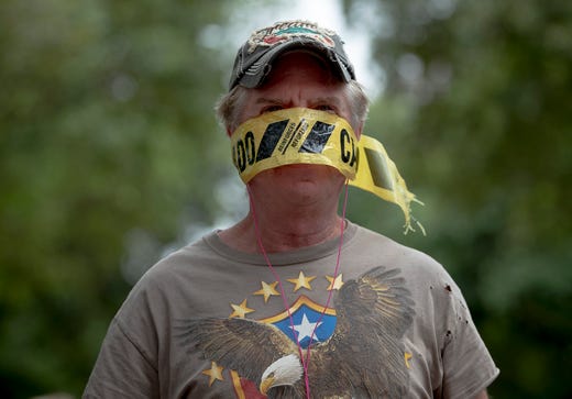 A man who declined to provide his name wears yellow caution tape as a mask during a protest in Texas on April 18, 2020.