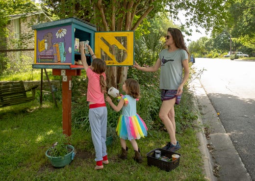 Sheila Parr and her daughters Violet Cann, left, 7, and Stella Cann, 5, donate food and toilet paper to the Little Free Library on Princeton Drive in Austin, Texas, on Tuesday April 21, 2020.  In response to the coronavirus pandemic, many of the book exchange boxes around the U.S. are being repurposed as sharing boxes with free food and toilet paper. 