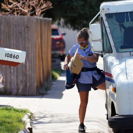 U.S. Postal Service carrier Amy Bezerra loads mail, including an Amazon package, into her delivery pouches along her route in suburban Denver.