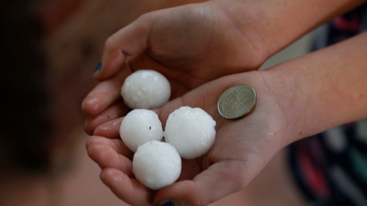 A person holds hail and a quarter to show scale during a storm in Tulsa, Okla. Wednesday, April 22, 2020.
