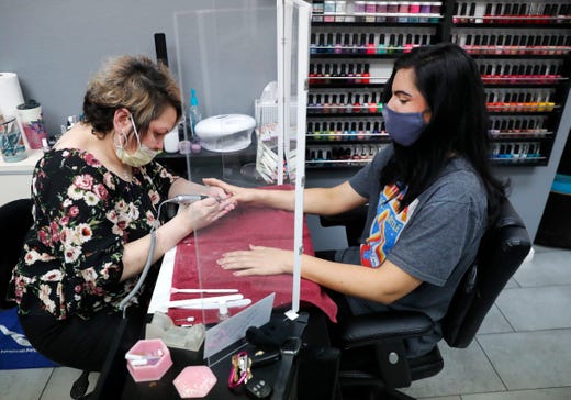 Manicurist Rhonda Simpson, left, polishes nails for her customer Faith at the reopened Salon A la Mode in Dallas, Friday, April 24, 2020. The salon installed a barrier between the two to avoid the spread of coronavirus.