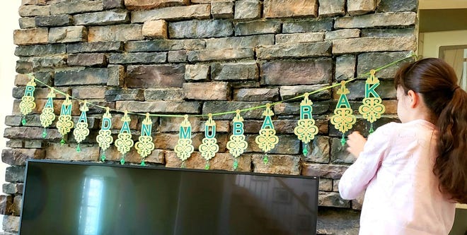 Najwa Awad's daughter, Safiya Helmi, 8, puts up a Ramadan Mubarak banner as a part of her family's decorations for the holiday.