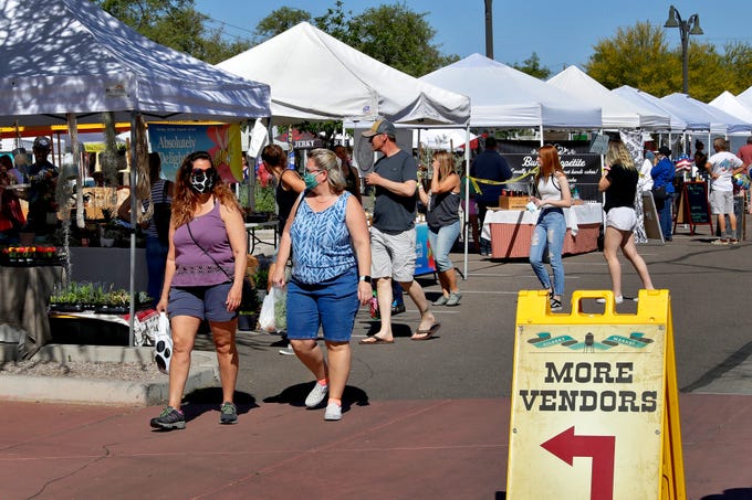 People wear masks to prevent the spread of coronavirus as they walk through the farmers market Saturday, April 25, 2020, in Gilbert, Ariz. The new coronavirus causes mild or moderate symptoms for most people, but for some, especially older adults and people with existing health problems, it can cause more severe illness or death.