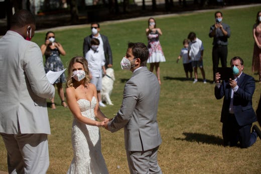 Gabrielle Schmees, 29, and Diego Grassano, 31, get married wearing protective masks at the Gerald D. Hines Waterwall Park on Monday, April 27, 2020, in Houston. Their friend Torrance Wilson officiates the wedding. Because of COVID-19, the couple decided to postpone their official wedding and have a small one at the Waterwall Park until December when they can have the official one with all of their family and friends.