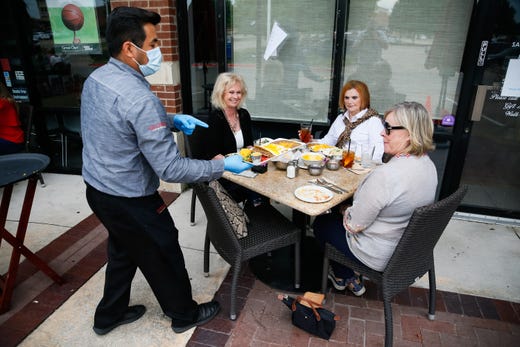  A waiter at Gloria's Latin Cuisine in serves up lunch to patrons seated on the patio in Colleyville, Texas on April 27, 2020.