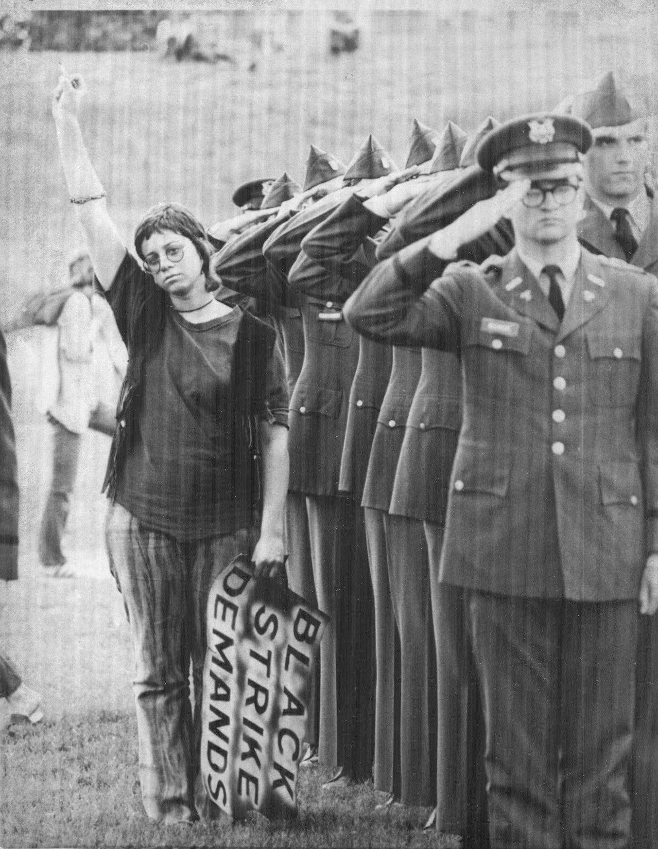 An unidentified demonstrator at Ohio State University defies the Nation Anthem and doubles her fist as members of the school's ROTC unit salute during ceremonies. May 5, 1970.