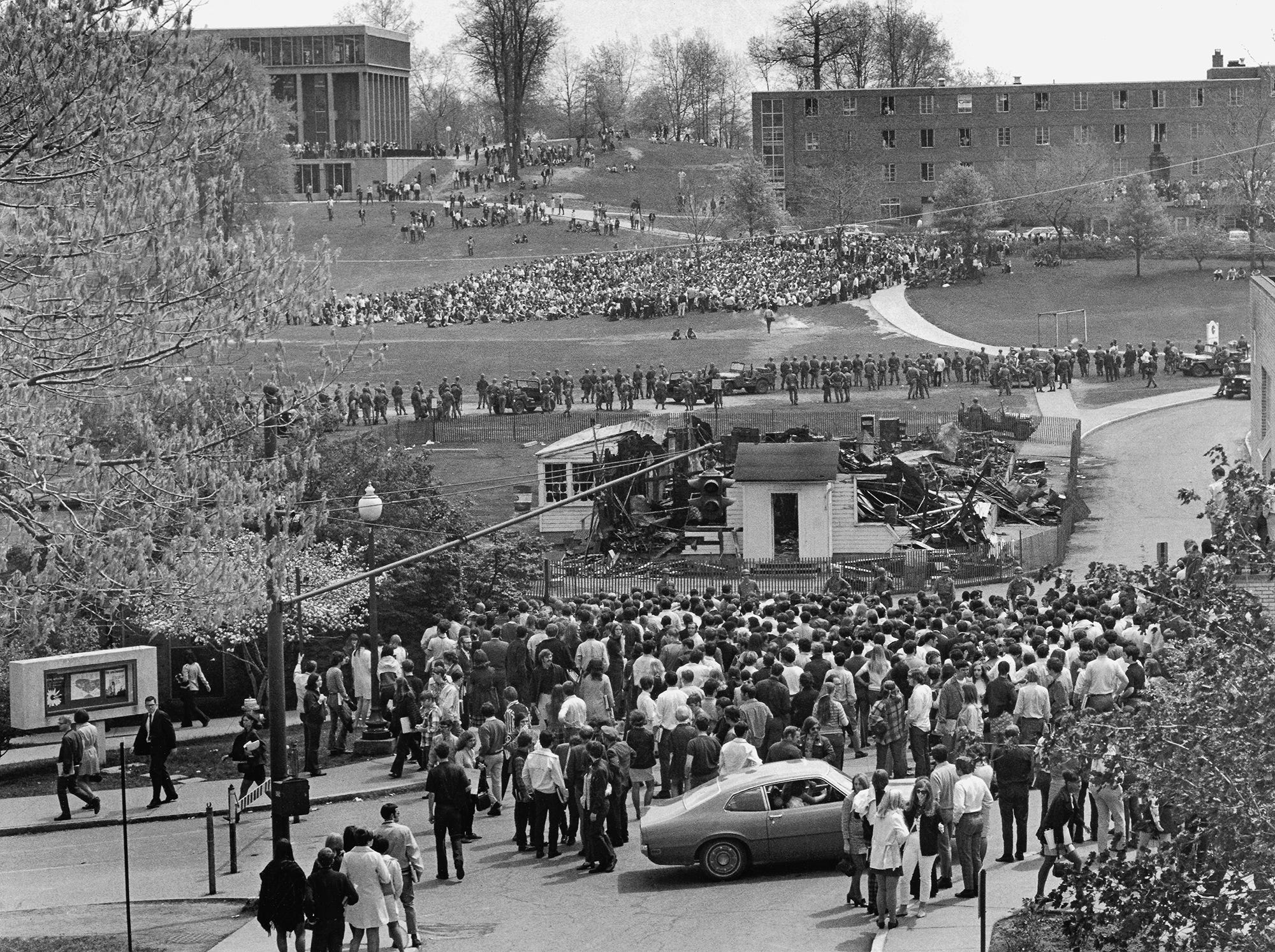 A crowd of students, some carrying their books gathers near the charred remains of the ROTC building on the Kent State campus. At the top left is Taylor Hall, where, around noon on the building’s far side, National Guardsmen clashed with protesters and opened fire.