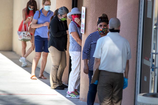 As the heat outside rises, people try to stand in the shade while waiting to enter a bank on Highway 111 in Rancho Mirage, Calif., on Monday, May 4, 2020.