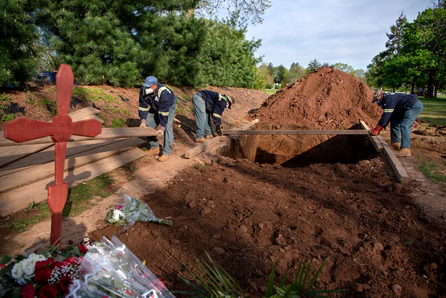 Cemetery workers lay planks of wood across three freshly dug grave sites at East Ridgelawn Cemetery in Clifton in preparation for three burials to take place on May 5, 2020. During an average April the cemetery performs 45 burials, but during the coronavirus pandemic they performed one hundred and forty-eight.