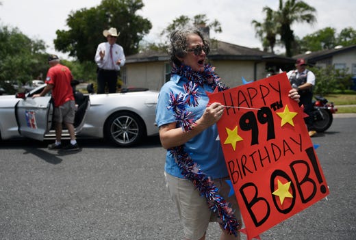 Cassandra Champion holds a happy birthday sign for Bob Batterson during his surprise, drive-parade, Friday, May 8, 2020. Cars drove past the 99 year old's home. 