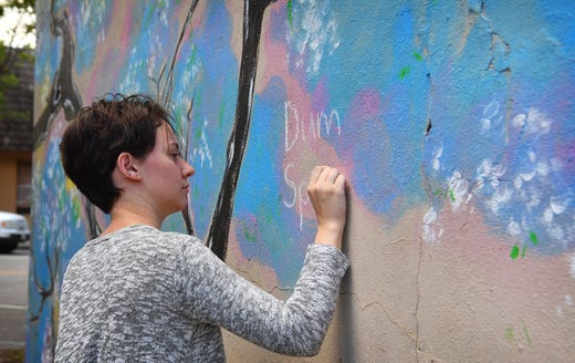 Alex Lewis writes in Latin, Dum Spiro Spero, or "While I breathe, I hope", on the Mural of Hope painted by Gaya Khmoyan at Backdoor Theatre Friday.