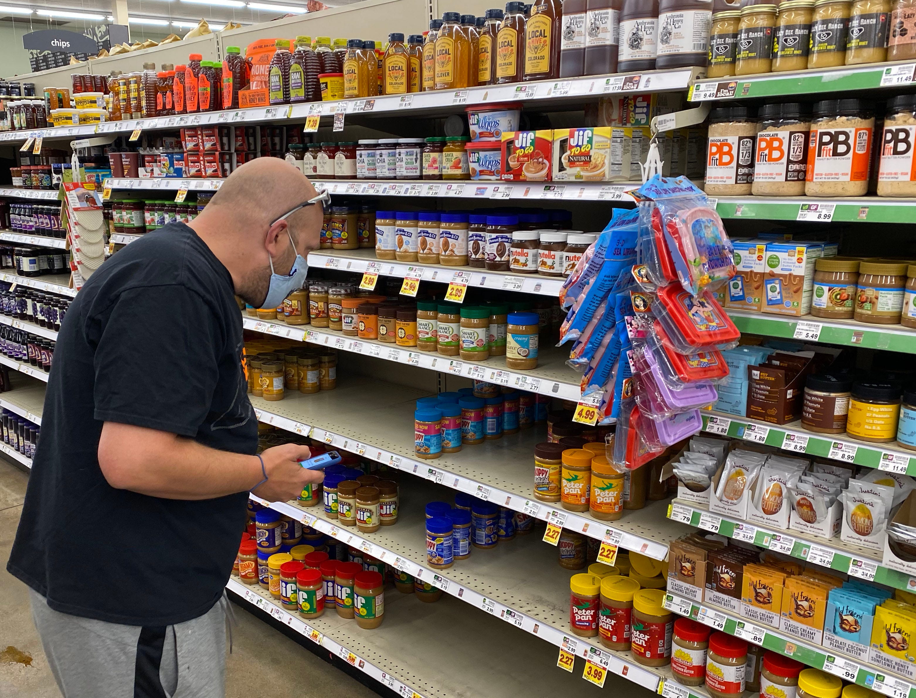 Instacart shopper Jeff Mitchell scans the shelves for the correct kind of peanut butter ordered by a customer inside a grocery store in Boulder County, Colorado.