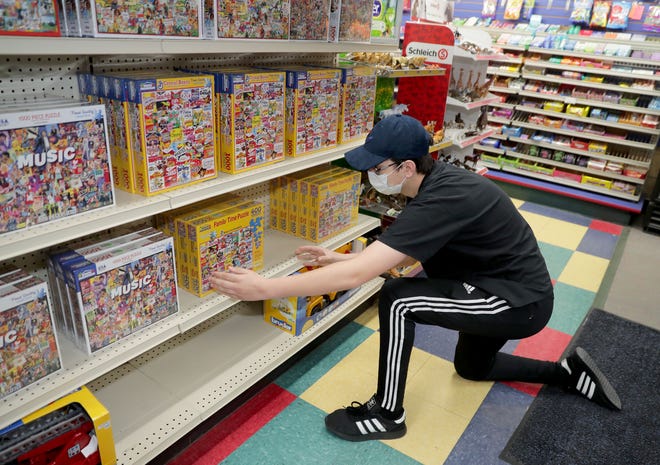 Employee Jack Stuhlmacher adjusts some puzzles on a shelf at Winkie’s Toys and Variety in Whitefish Bay, which is among the area businesses that have reopened.