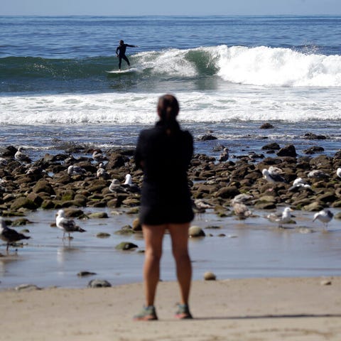 A visitor watches surfers from the shore on Topang