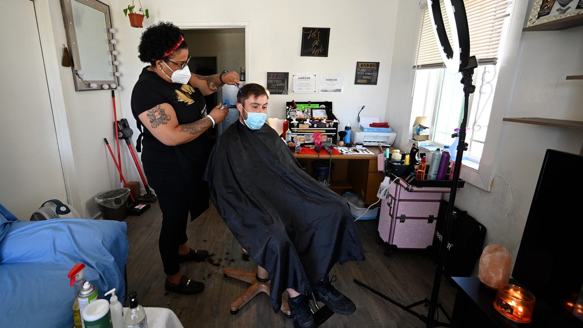 Carmelle Harris gives client John Batinovic a haircut in the living room of her home on May 14, 2020 in Compton, Calif. Harris is one of many hairstylists working in violation of the California stay-at-home order. Harris is cutting hair at home and other hairstylists are making "house calls" as the hair industry tries weather the storm during the pandemic.