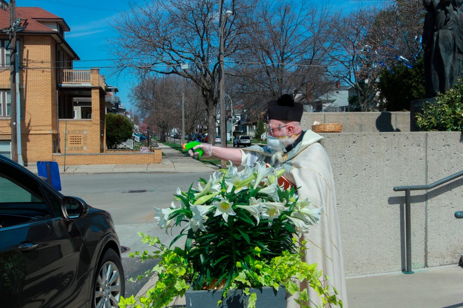 In this Saturday, April 11, 2020, file photo, Rev. Timothy Pelc blesses Easter baskets outside St. Ambrose Church in Grosse Pointe Park, Michigan. Pelc, wearing church vestments and protective gear, offered a prayer and sprayed holy water from a squirt gun instead of blessing baskets inside the church in a bid to maintain social distancing during the coronavirus pandemic.