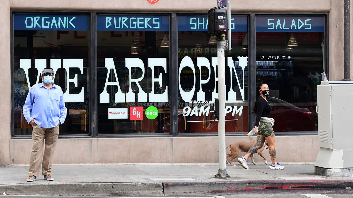 Pedestrians wear facemasks in front of a restaurant in Los Angeles, California on May 12, 2020, as Governor Gavin Newsom announced guidelines for reopening of restaurants, with self-distancing and cleanliness procedures as the state's coronavirus pandemic.
