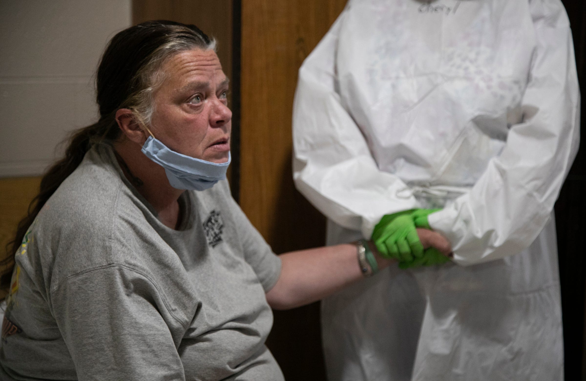 Marsha Roderick, 50, left, has her hand held by case manager Cheryl Linari before Dr. Neeli Thati administers a nasal swab to test for COVID-19 Friday, May 8, 2020 in her room at Salvation Army Harbor Light in Detroit. Salvation Army Harbor Light in Detroit has set up wings in its facility to take on testing and some treatment of COVID-19 positive and pending.