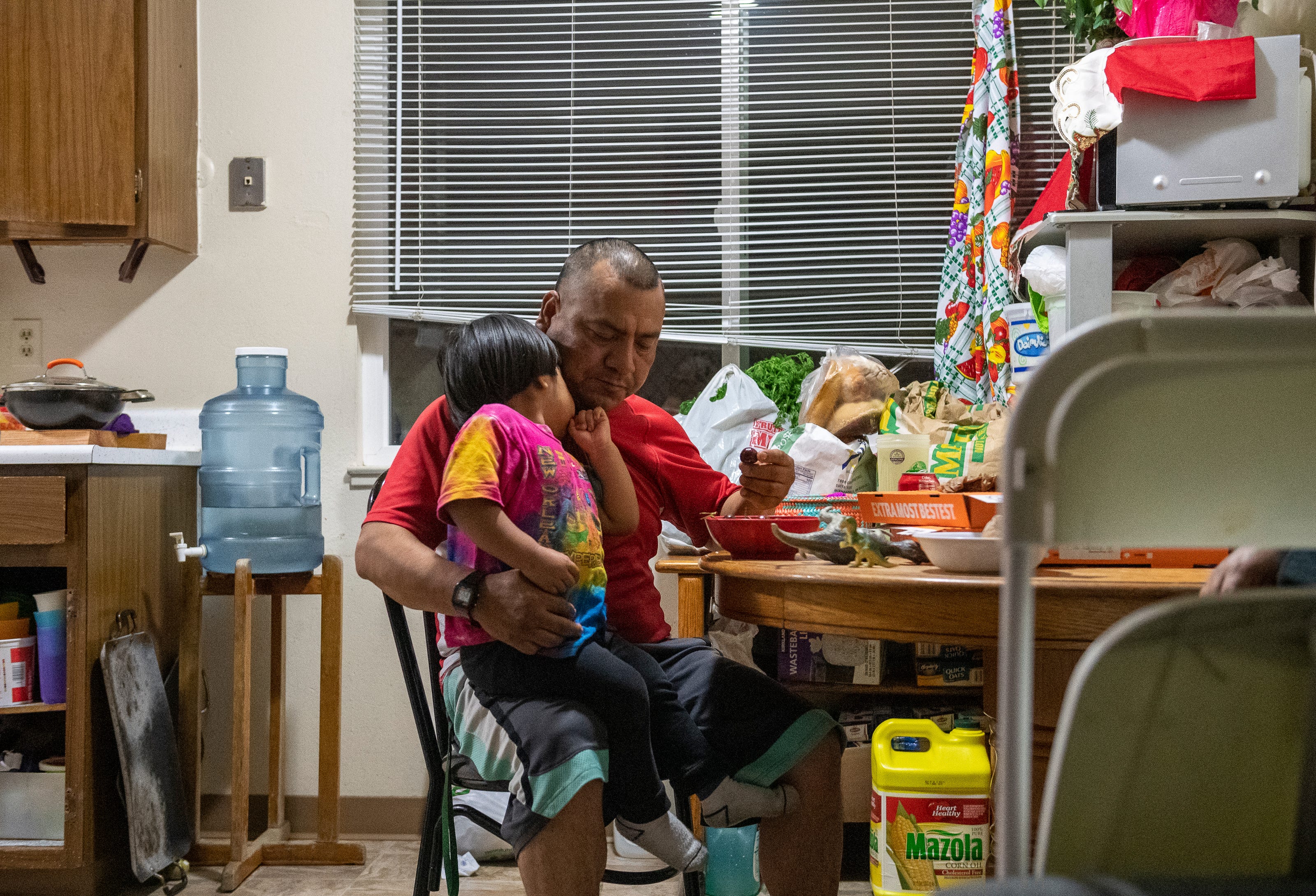 Jesus Salvador, left, tucks his head into his father Meliton's neck, as Meliton eats a cherry inside their two-room apartment on the north side of Salinas on May 16.