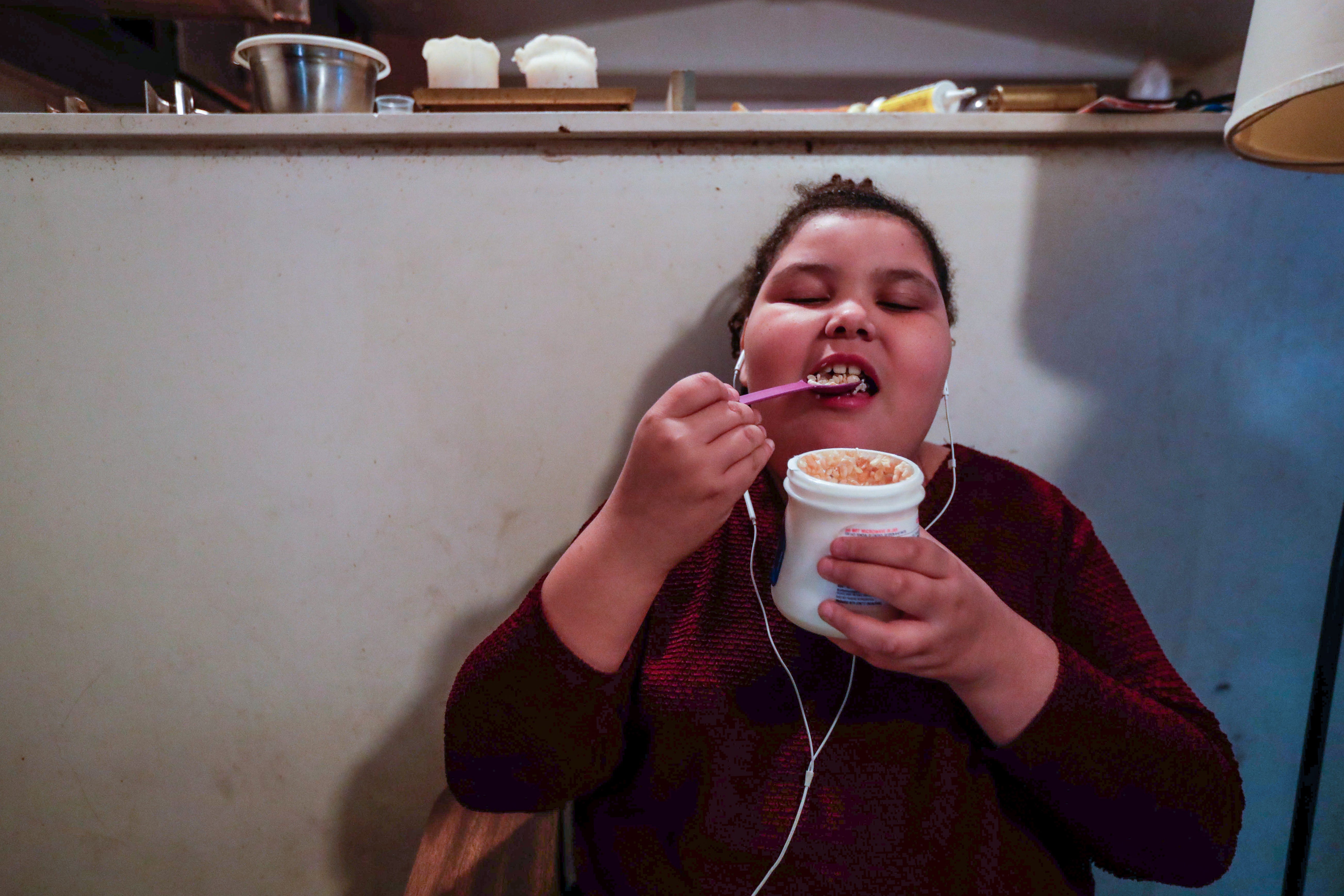 Vivianna Hughes, 9, sits at a school desk in the living room of the family's mobile home while eating marshmallow fluff and Rice Krispies cereal as an afternoon snack. A cockroach scurries along the ledge of the counter above Vivanna's right shoulder.