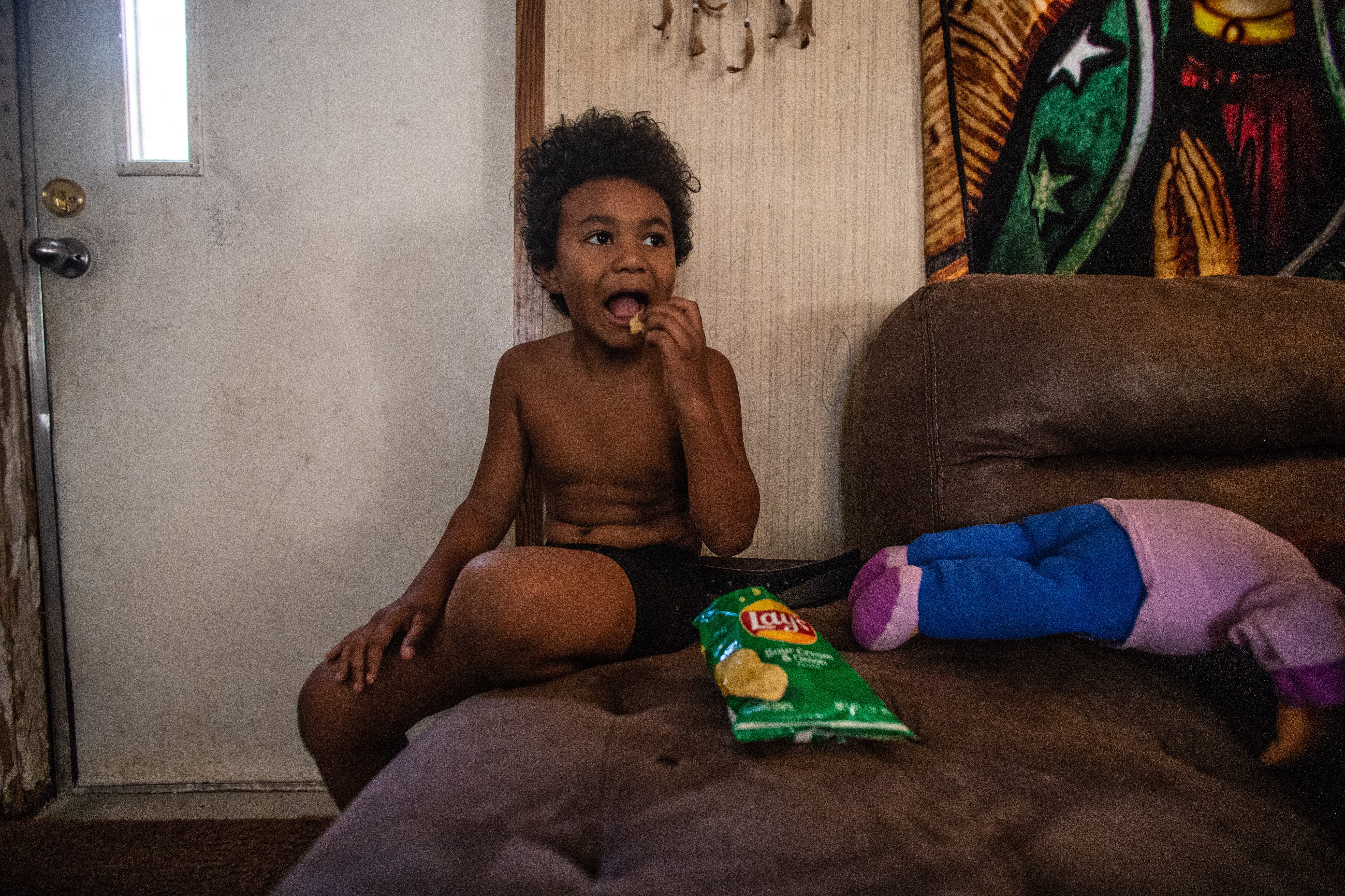 Romeo, 8, eats sour cream-and-onion chips on the living room couch in his mobile home off Aenon Church Road.