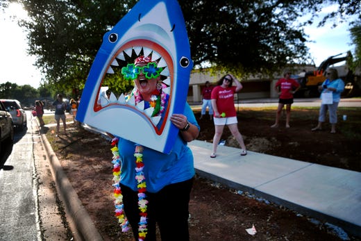 Kindergarten teacher Kathy Giron waves a shark mouth cutout as she calls to a passing student outside of Austin Elementary School Tuesday May 19, 2020. Students of all grades paraded by to say goodbye to their teachers at the end of the school year which had been severely altered due to the coronavirus pandemic. Since mid-March, students have only been able to interact with their teachers over online teleconference services and virtual classrooms.
