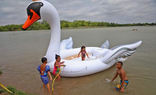 Young people flock around a large inflatable swan anchored to the shore at Lake Nasworthy during Memorial Day weekend on Saturday, May 23, 2020.