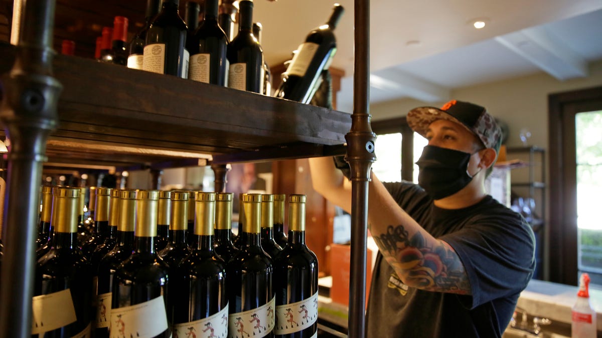 Jesse Cierly stocks a tasting bar shelf with bottles of wine at the Francis Ford Coppola Winery in Geyserville, Calif. The winery has been closed the past two months because of the coronavirus threat and is preparing to reopen to visitors.