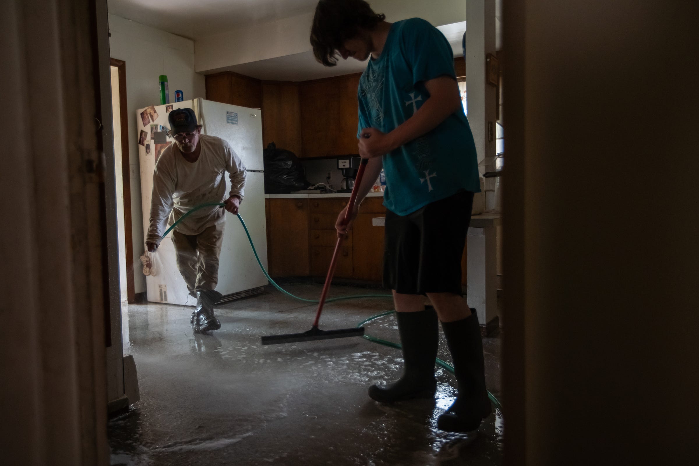 Jim Mcguire of Sanford sprays water from a hose across his kitchen floor as his son Robert Mcguire pushes the water down the steps into their flooded basement on Friday, May 22, 2020.