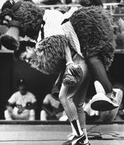 In this July 12, 1983, file photo, the Phillie Phanatic jumps onto the back of Atlanta Braves catcher Biff Pocoroba, who didn't see the Phillies mascot coming a warmup before a baseball doubleheader in Philadelphia.