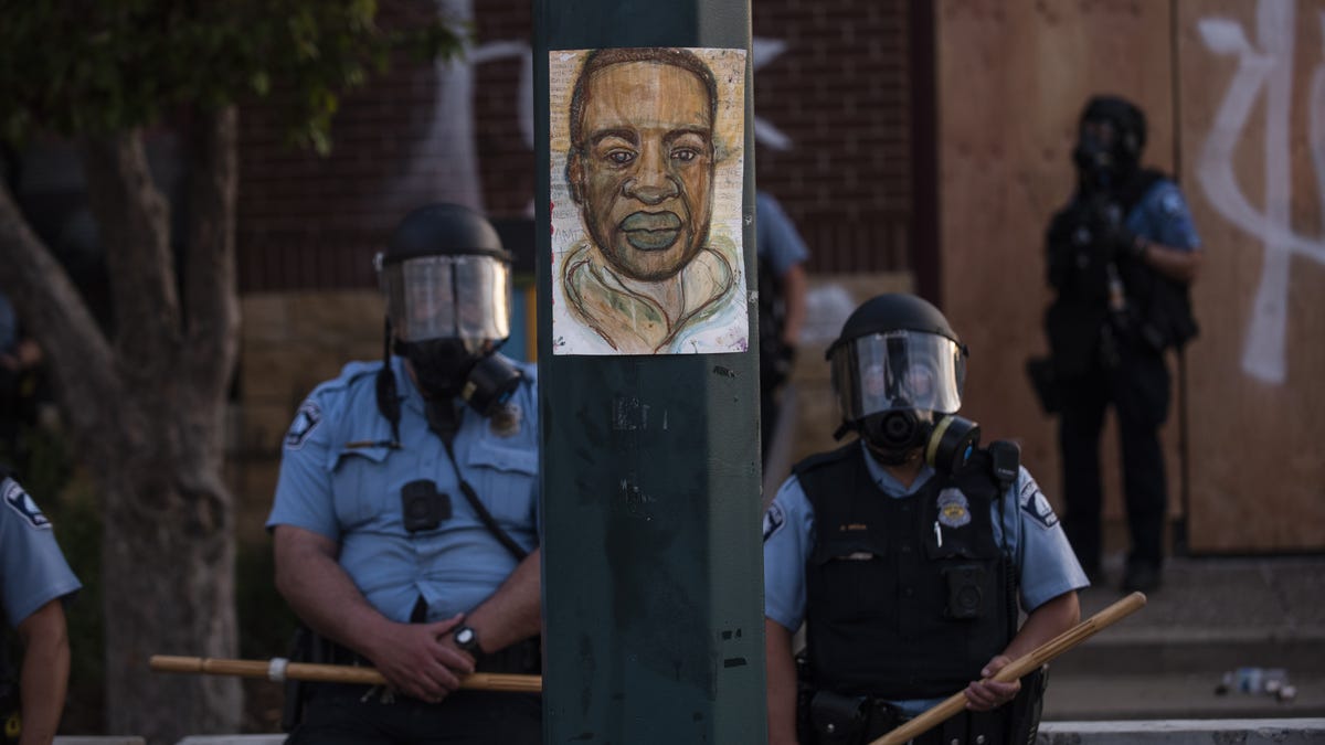 A portrait of George Floyd hangs on a street light pole as police officers stand guard at the Third Police Precinct during a face off with a group of protesters on May 27, 2020 in Minneapolis, Minnesota.  The station has become the site of an ongoing protest after the police killing of George Floyd. Four Minneapolis police officers have been fired after a video taken by a bystander was posted on social media showing Floyd's neck being pinned to the ground by an   officer as he repeatedly said, "I cant breathe". Floyd was later pronounced dead while in police custody after being transported to Hennepin County Medical Center.