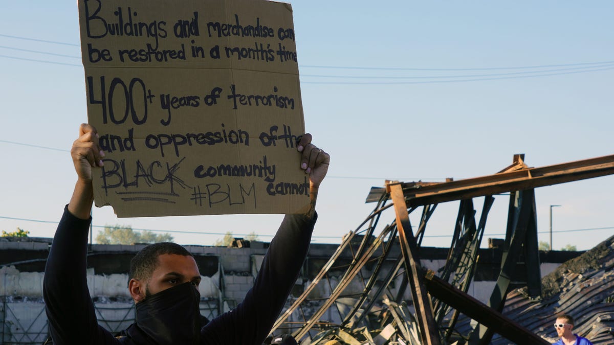 A protester holding a sign in front of a burned-out building Minneapolis during protests over the death of George Floyd on May 28, 2020. 