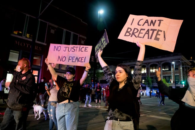 Protestors hold up signs while confronting police in OTR on Friday night. The protest started in response to the death of George Floyd.