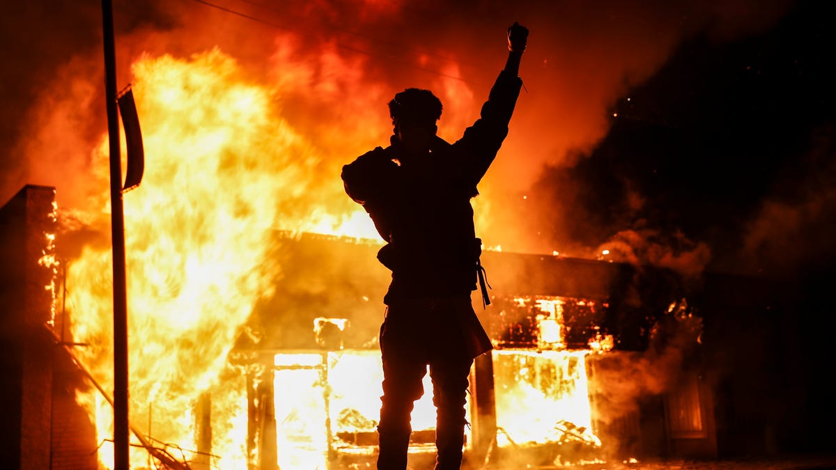 A demonstrator stands beside a fire of a building that was once a check cashing business, Saturday, May 30, 2020, in St. Paul, Minn. Protests continued following the death of George Floyd, who died after being restrained by Minneapolis police officers on Memorial Day. 