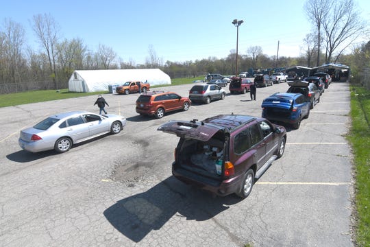 Dozens of cars arrive with their trunks and hatchbacks open as volunteers prepare to load cases of bottled water, milk and produce at the Greater Holy Temple parking lot in Flint on Thursday, May 7, 2020. 