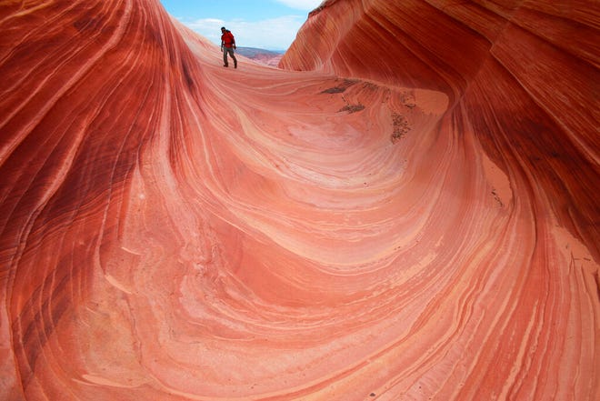 FILE - In this May 28, 2013, file photo, a hiker walks on a rock formation known as The Wave in the Vermilion Cliffs National Monument in Arizona. A walk-in lottery for the popular Arizona hike could move online. Half of the 20 permits for one of the most exclusive and dramatic hiking spots in the southwestern United States remain unavailable during the coronavirus pandemic. The virus hasn't forced the closure of the Wave in the Vermillion Cliffs National Monument along the Arizona-Utah border. But it has suspended a daily, in-person lottery for 10 permits because the agency that oversees it can't ensure social distancing. (AP Photo/Brian Witte, File)