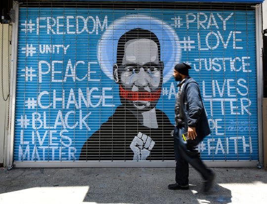 A man walks past a protest mural on a closed business on in Los Angeles.