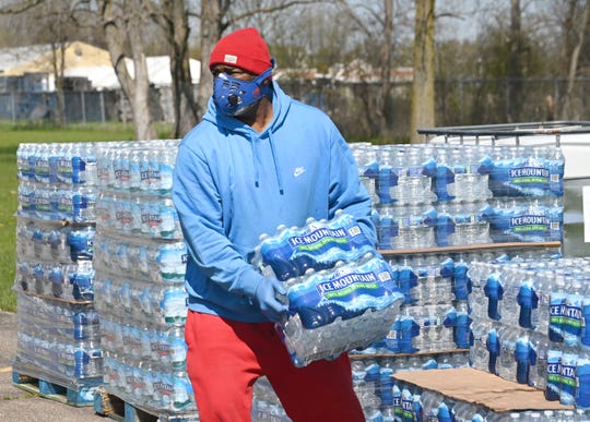 Volunteer Arthur Woodson, R.L. Community Outreach Center, carries cases of water at the Greater Holy Temple as the mobile food pantry distribution loaded vehicles for resident in need in Flint.