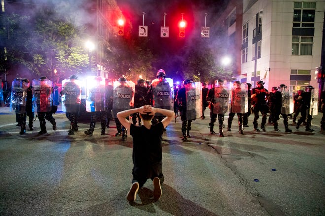 Riot police approach a protester kneeling on Central Avenue in Cincinnati, Ohio, blocking in OTR in the early hours of Saturday, May 30, 2020.  In this image police had cleared a crowd using flash bangs, one protestor refused to leave and got on his knees in front of police. He moved right before riot cops got to them. The protest started in response to the death of George Floyd.