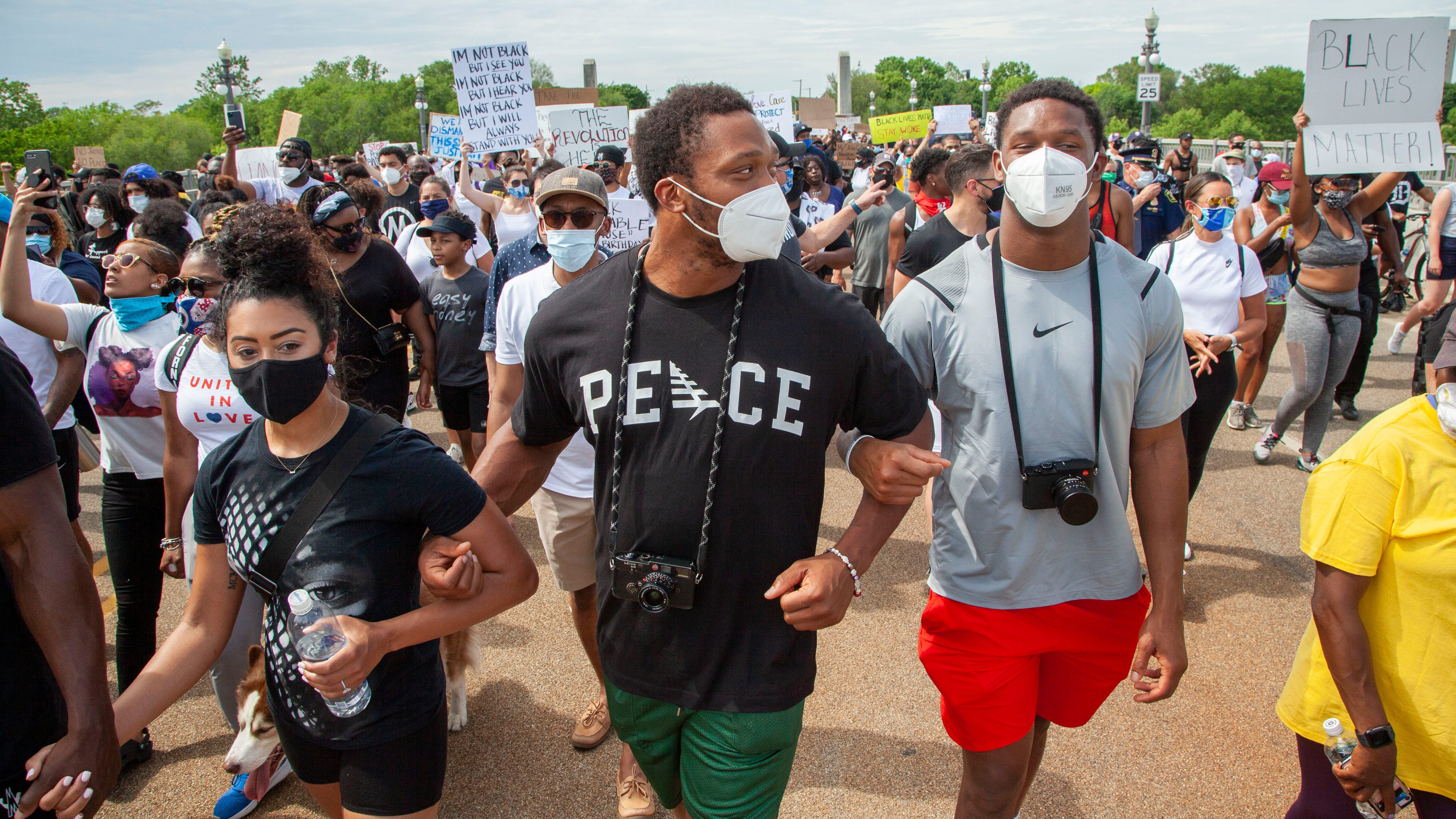 Detroit Lions player, Romeo Okwara, center, and his brother Julian, right, lead protesters arm and arm as they march across the MacArthur Bridge across the Detroit River to and from Belle Isle during a rally in Detroit, Friday, June 5, 2020, protesting police brutality and the death of George Floyd.