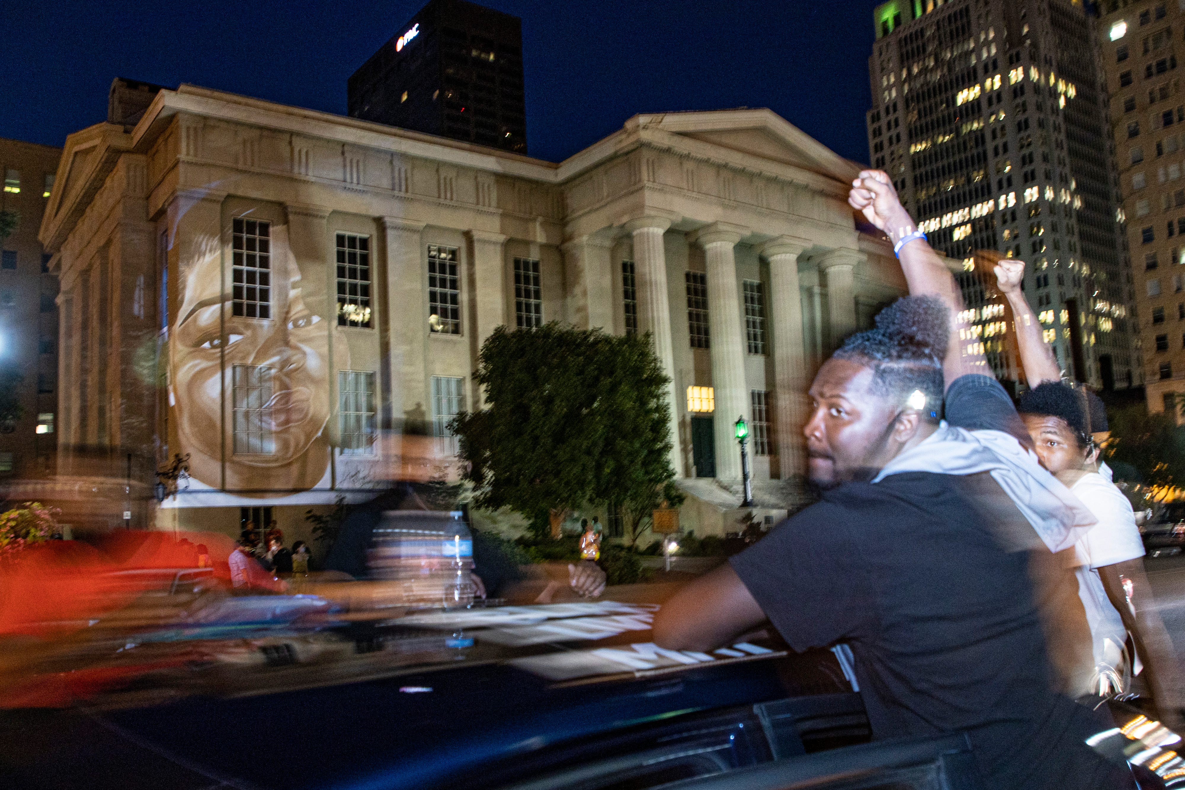 Protesters drive past a portrait of Breonna Taylor, made by local artist Jaylin Stewart, is projected onto Metro Hall during a celebration and protest of police brutality and justice on what would have been the 27th birthday of Breonna Taylor in Louisville. June 5, 2020