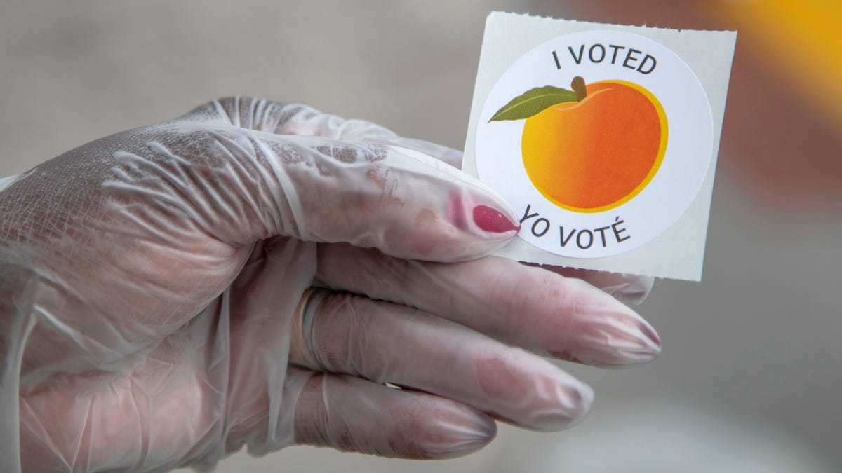 An early voter, who wore gloves to cast their ballot, shows off their sticker during Georgia's primary election at the Gwinnett County Voter Registration and Elections Office in Lawrenceville, Georgia, May 18, 2020.