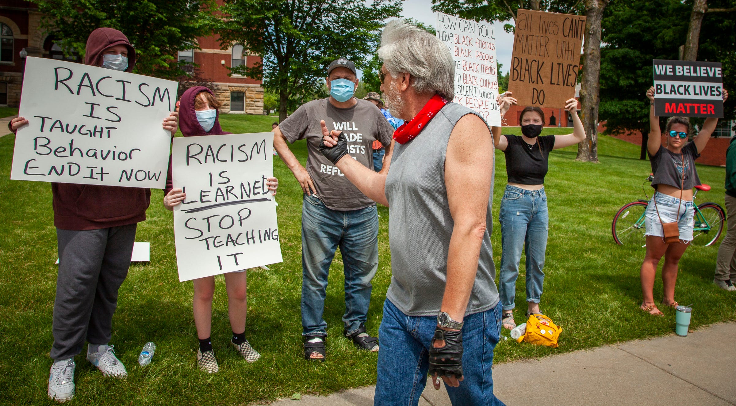 A man walks along the line of protesters with a raised middle finger as they hold their signs up in front of the historic courthouse in downtown Howell, Michigan as a large crowd came out June 4, 2020 to protest against police brutality and racism did come out to hold signs and rally.