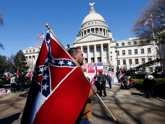 In this Jan. 19, 2016 file photo, Hjalmberi Shytox of Purvis, Miss., carries a Mississippi state flag in front of the Capitol in Jackson, Miss., while participating in a rally in support of keeping the Confederate battle emblem on the state flag.